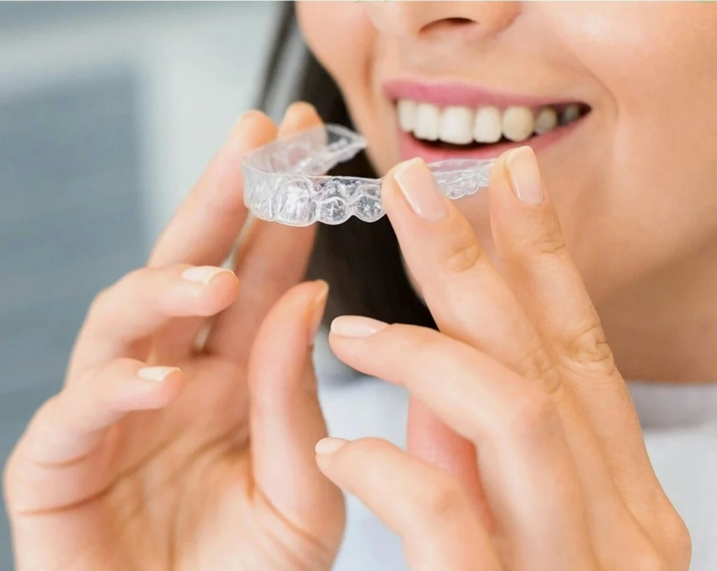 A woman holding Invisalign aligners with a bright smile on her face.